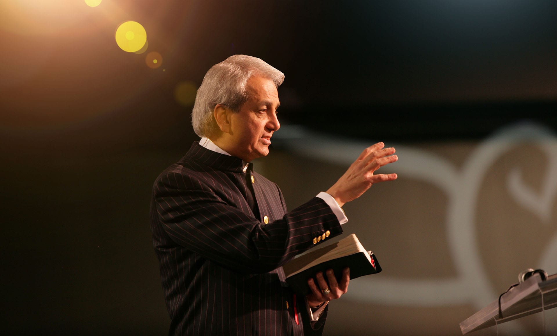 Pastor Benny Hinn Teaching at a conference with dove logo in the background